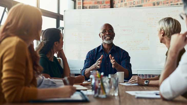 Man talking to people around a table and in front of white board