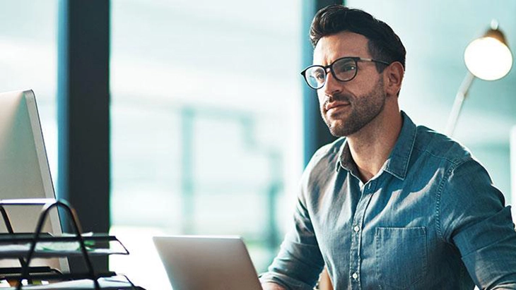 Man with glasses sitting at lap top reflecting