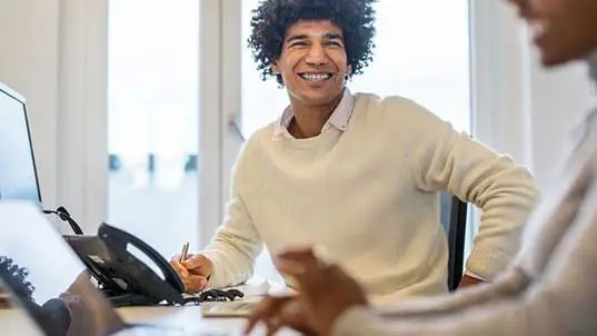 Man at desk in work space talking to colleague 