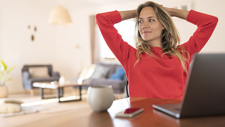 Woman sitting at desk and leaning back with hands behind head and smiling