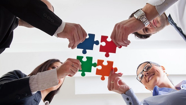 Colleagues holding 4 jigsaw pieces and connecting them