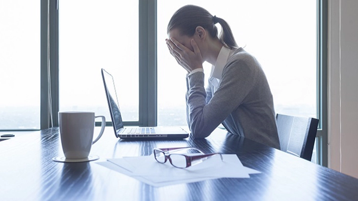 Women at desk working on laptop and with head in hands