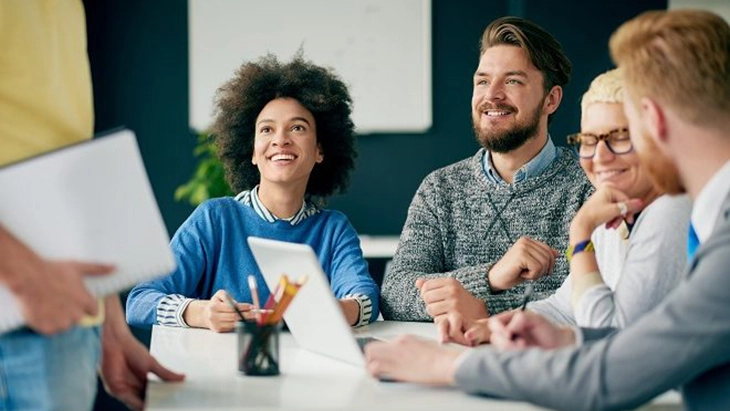 Diverse group of people sat around an office table, smiling and laughing