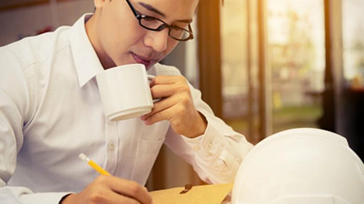 Man at desk writing and drinking a cup of tea 