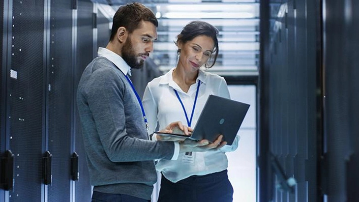 Man and woman standing and looking down at laptop the man is holding