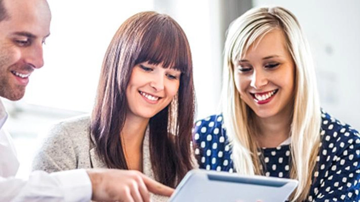 Man and two women looking down at computer screen 