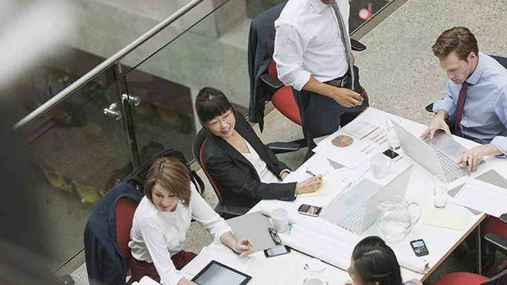 Overhead view of men and women working around table in office space