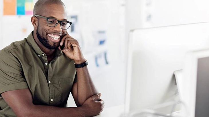 Man sitting at desk looking at computer and talking on phone