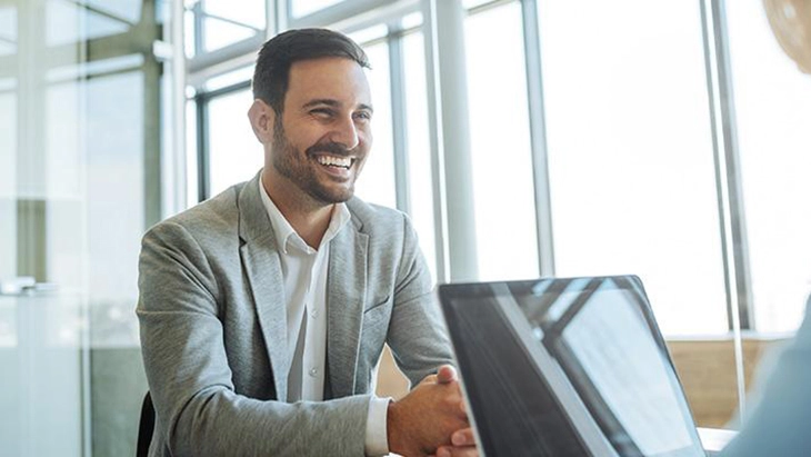 Man smiling at person across desk from him in work space