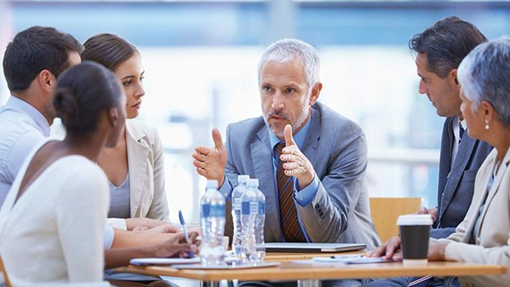 Distinguished-looking man speaking to male and female work colleagues around a table