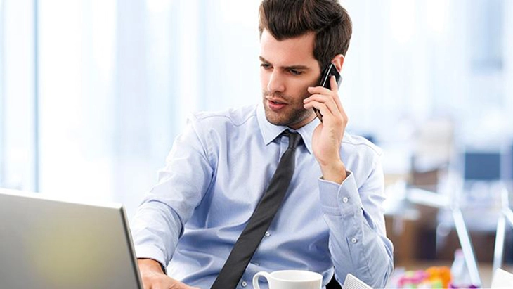 Man at desk looking at computer screen and talking on phone