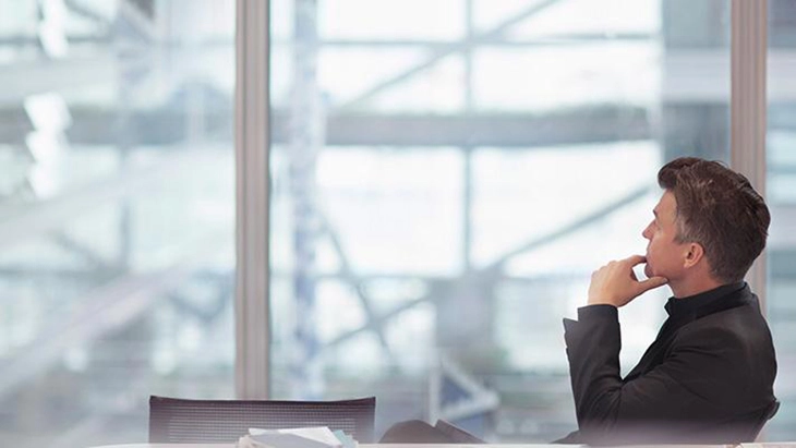 Man sitting with fingers on chin and looking out large window