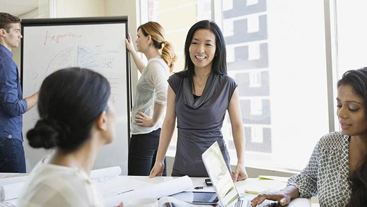 Four women and a man working in and office space