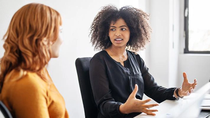 Two young women in workspace talking to each other