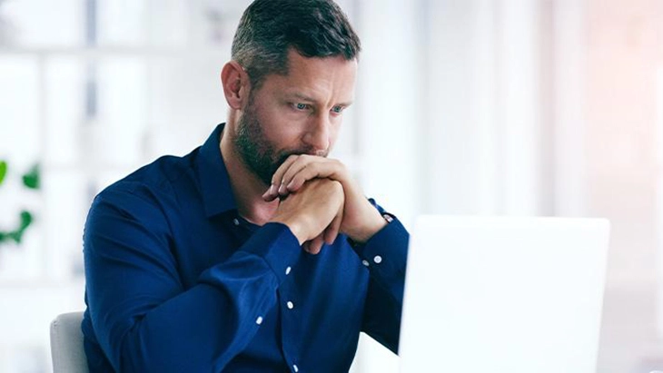 Man with elbows on table and chin on his hands looking at computer screen