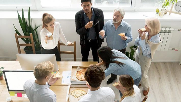 Men and women standing around a table eating takeaway pizza