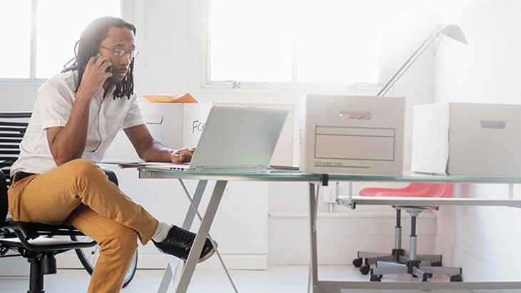 Man sitting at desk working on lap top and talking on phone