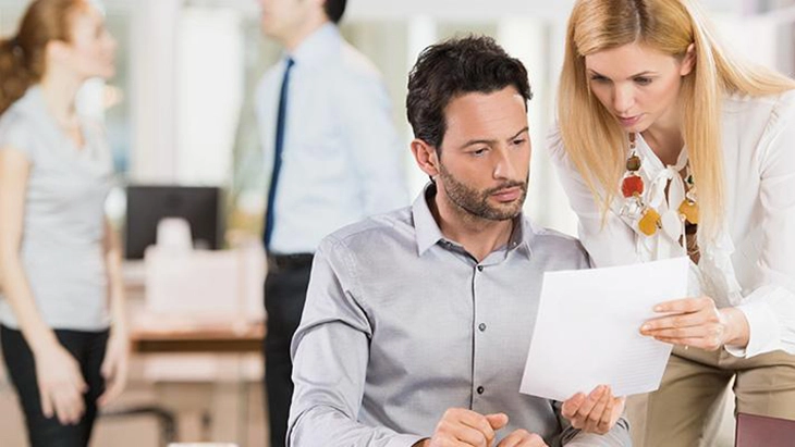 Woman holding sheet of paper in front of seated man