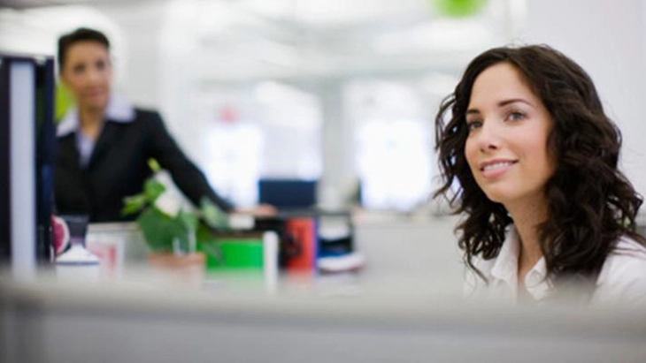 Young woman at workstation with colleague in background