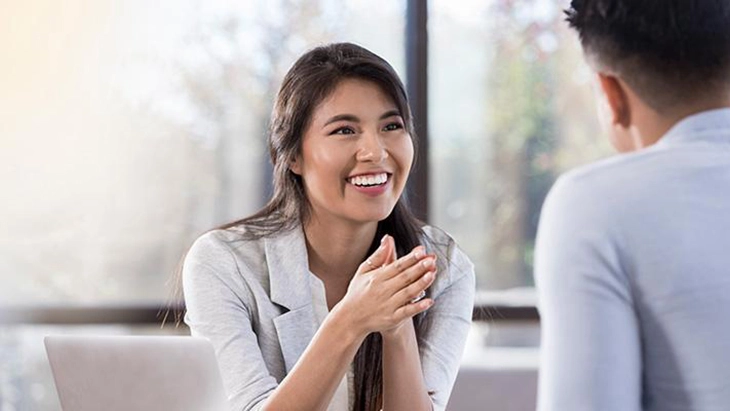 Young woman with palms together speaking to man in work space