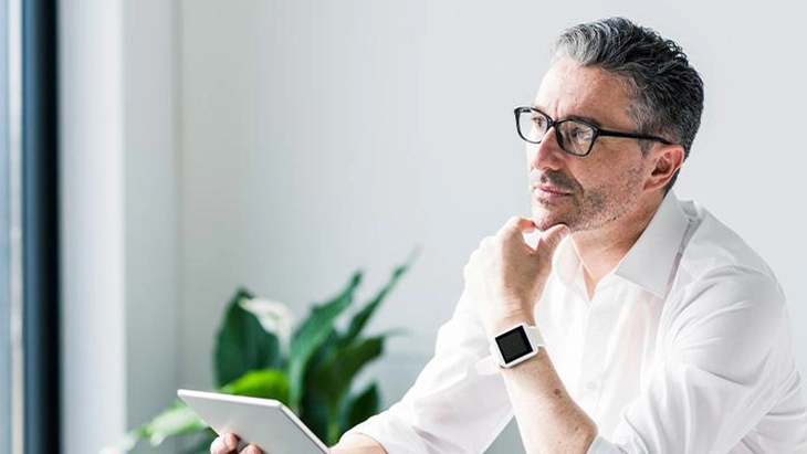 Man with glasses holding a tablet and thinking with fingers on chin