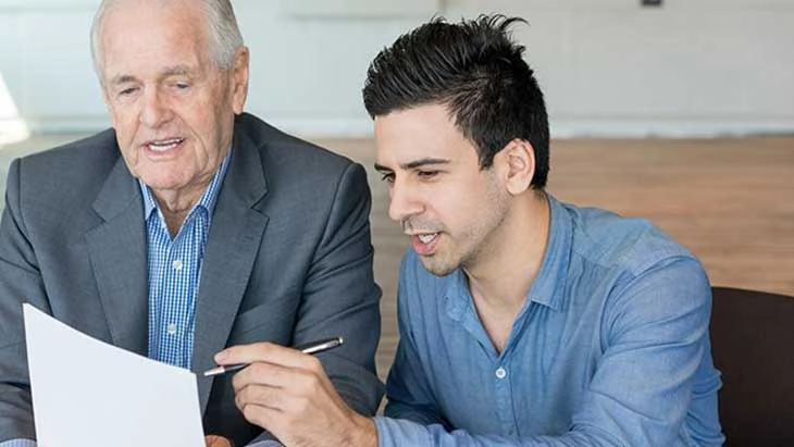 An older man and younger man reading and making notes on a sheet of paper