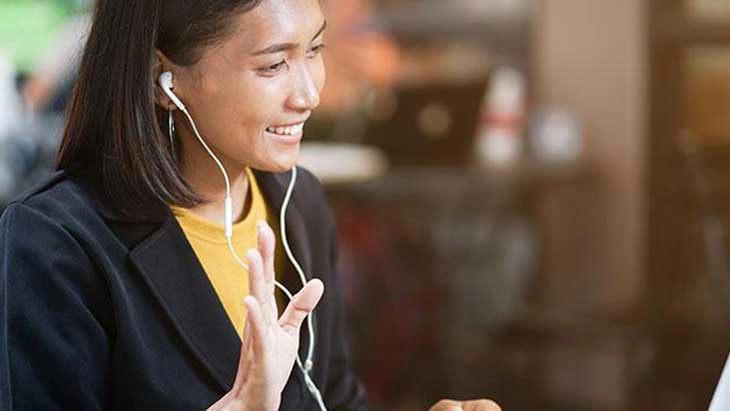 Woman in video interview wearing headphones, smiling and waving