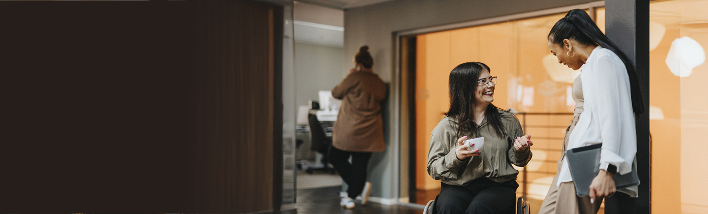 People in a modern office setting engaged in conversation and collaboration, illustrating developing people and managing talent in the workplace.