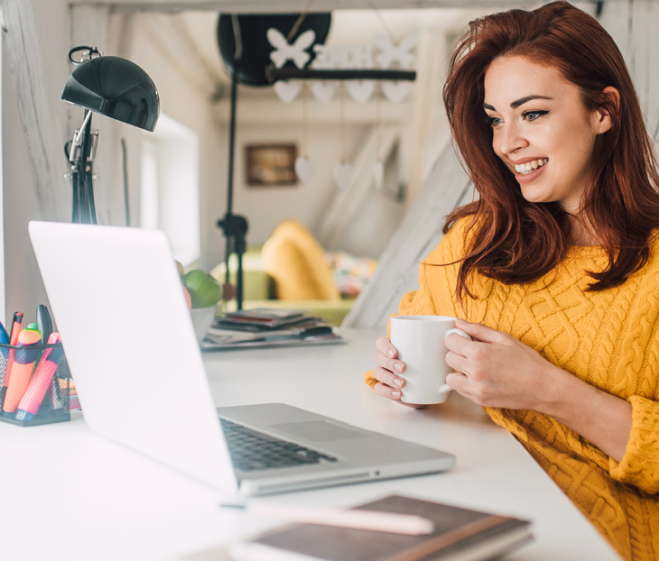 Women using laptop while sitting at a desk holding a mug