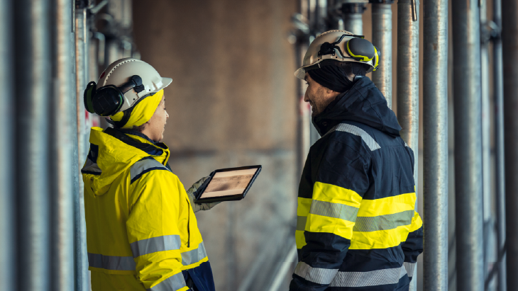 Engineers reviewing digital plans on a live infrastructure site, representing scalable workforce delivery and operational collaboration for Amey.