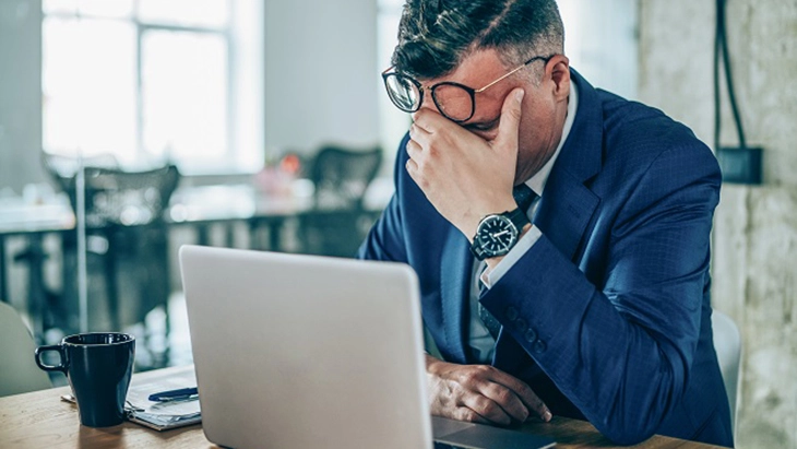 Man sitting in front of laptop with elbow on desk and face in hand