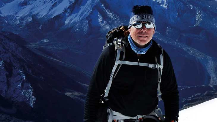 Man wearing sunglasses hiking through snowy mountains