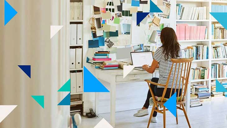 Woman sitting at desk and working on lap tap in room full of bookshelves
