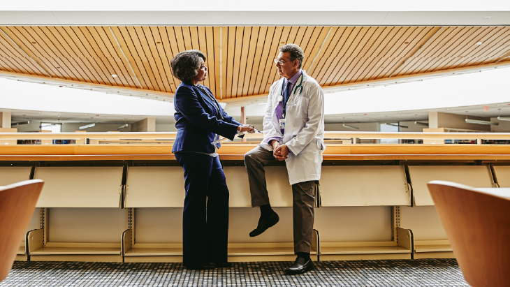 Two professionals in conversation inside a modern NHS hospital building, illustrating executive leadership collaboration during organisational transformation.