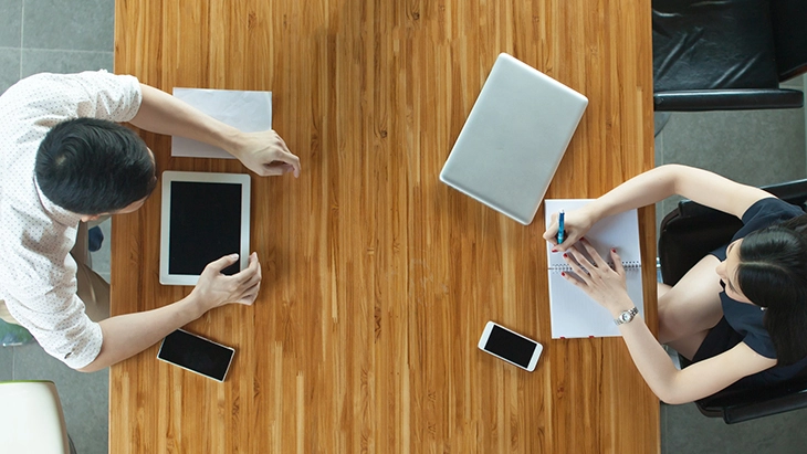 Aerial shot of a man and a woman sat opposite each other at an office desk.