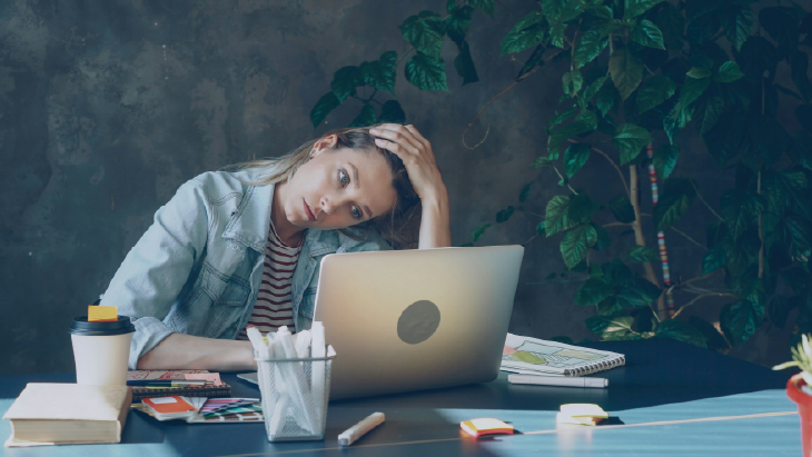 Person at desk with laptop, notebooks, and coffee cup in modern office, highlighting workplace mental health and support.