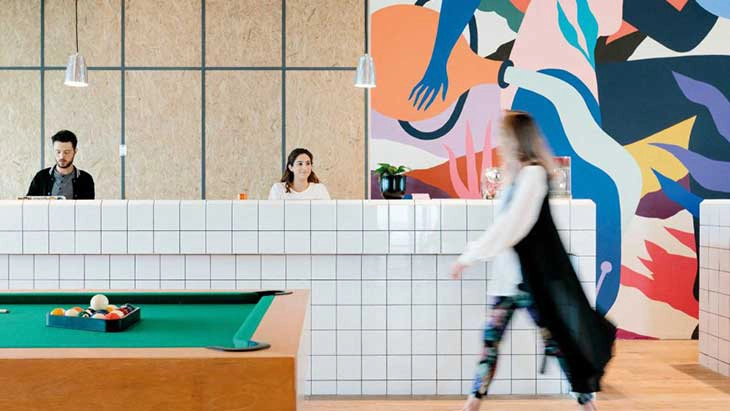 Man and woman at reception desk with pool table in front and modern art tableau behind