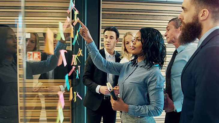 Woman placing post-its on mirror as colleagues watch