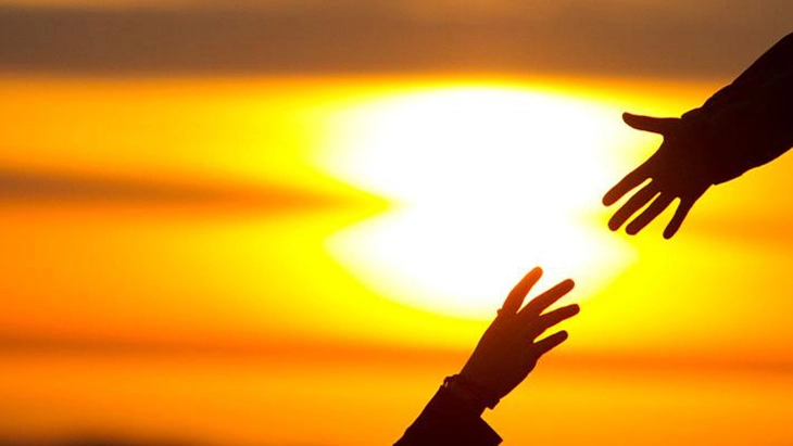 Two hands reaching out for each other in front of orange sky