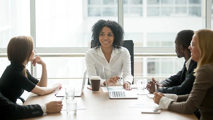 Woman sitting at head of table speaking with male and female work colleagues