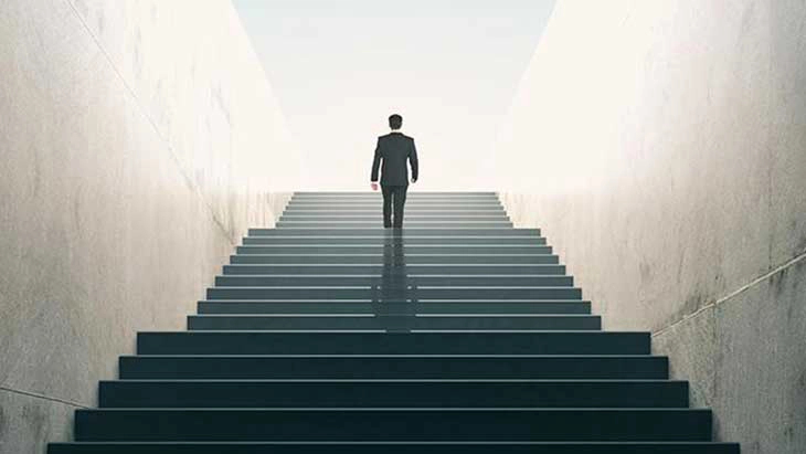 Man walking up stairs with high white walls on each side and sky above