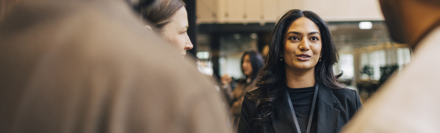 Banner for Hays UK Salary & Recruiting Trends 2026 leadership guide showing a person in a dark blazer with a lanyard, standing indoors with blurred figures in the foreground and office background.