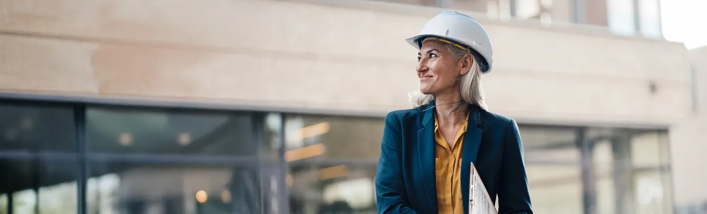 Construction professional wearing a hard hat and holding documents outside a modern building, representing insights from the construction and property workforce report.