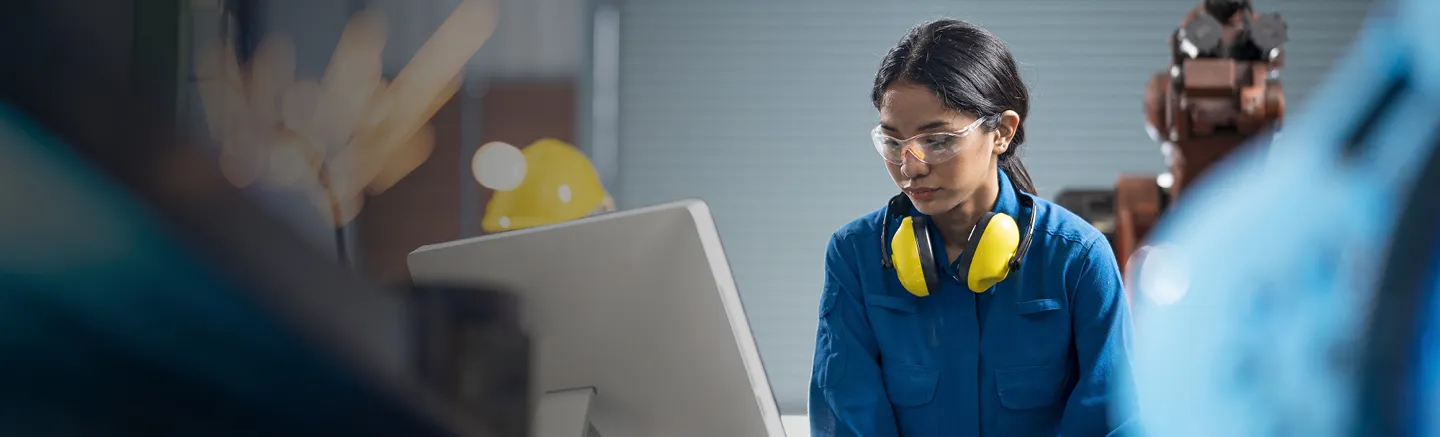 Engineer in blue protective workwear using a computer in an industrial setting, with safety glasses and hearing protection – representing engineering talent, workplace safety, and workforce insights.